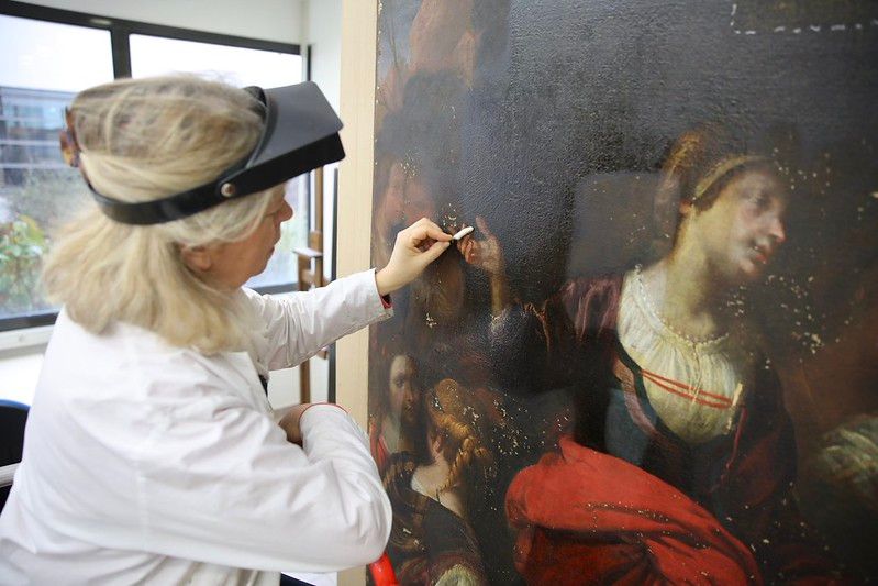 Un agent des Archives départementales œuvre à la restauration d'une peinture avec ses ustensiles.