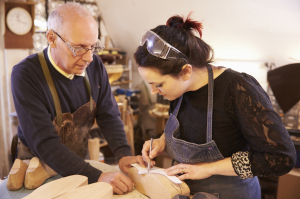 Senior shoemaker training apprentice to make shoe lasts